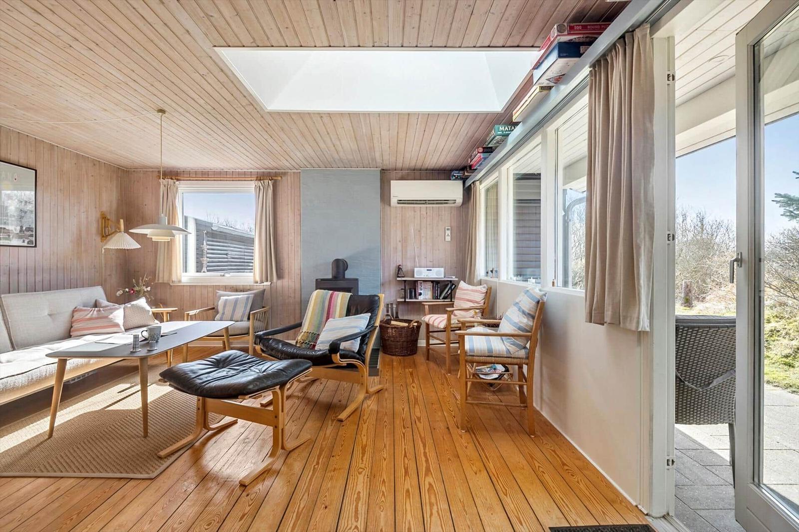 Wohnzimmer mit Holzboden, Sofa, Sessel und Terrassentür. Decke mit Dachfenster und Bücherregal.