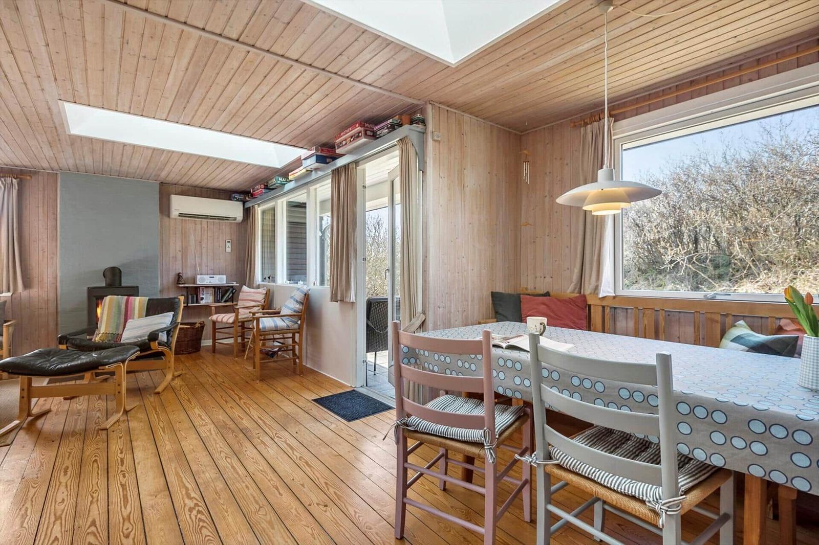 Ein Raum mit Holzdecke, Tisch mit Stühlen und Fenster. Es gibt einen Kamin und eine Tür.