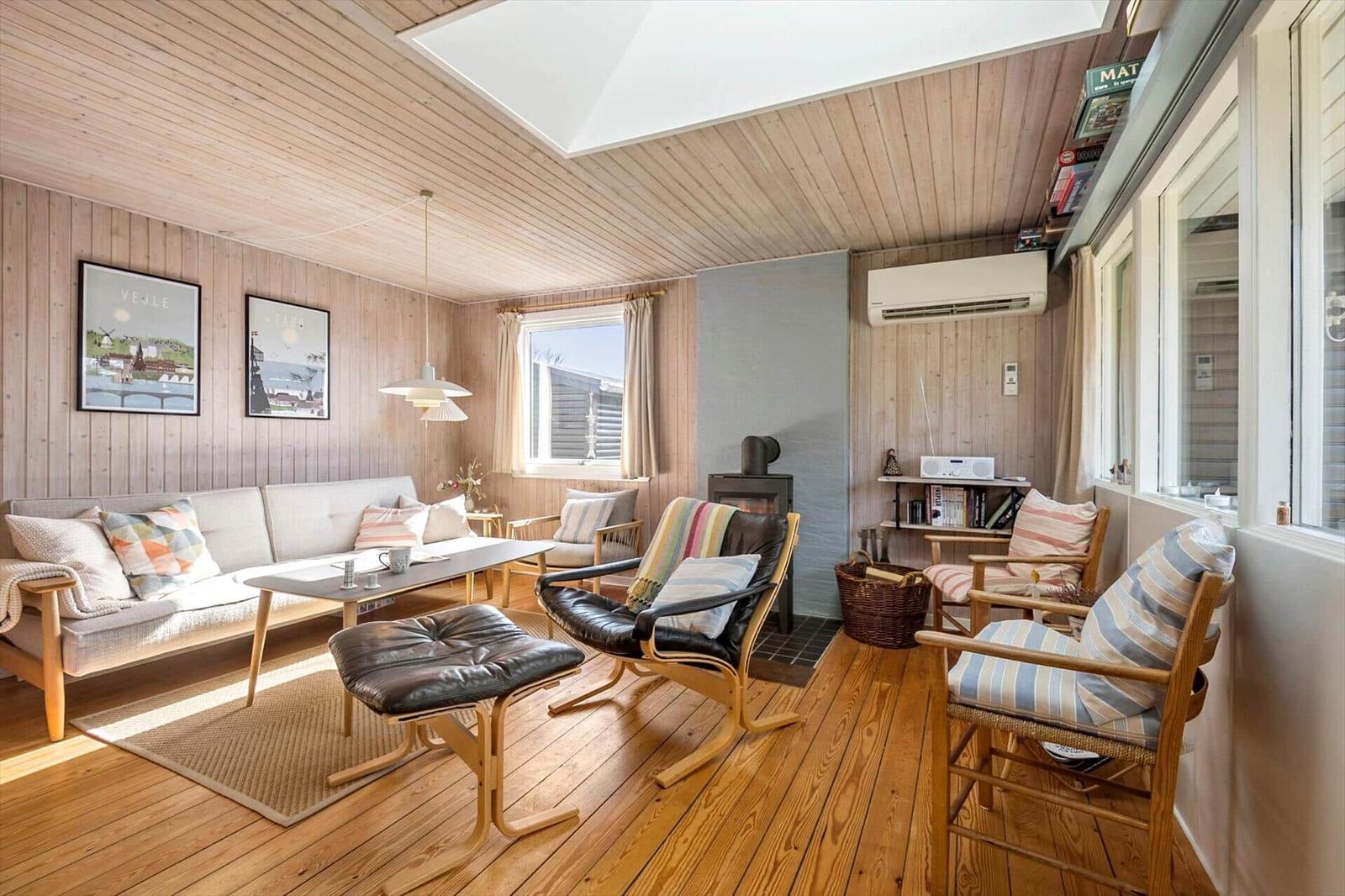 Wohnzimmer mit Holzwand, Sofa, Sessel und Kamin.