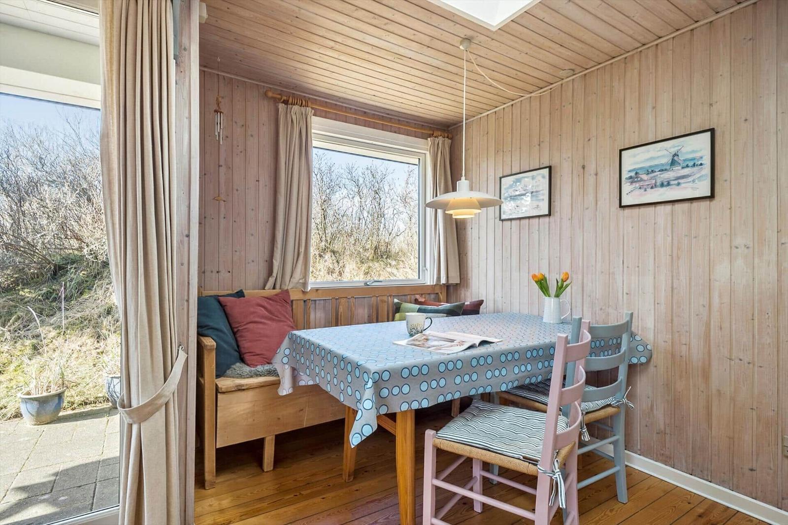 Esszimmer mit Holzwand, Tisch, Stühlen und Fensterblick auf Grünflächen.