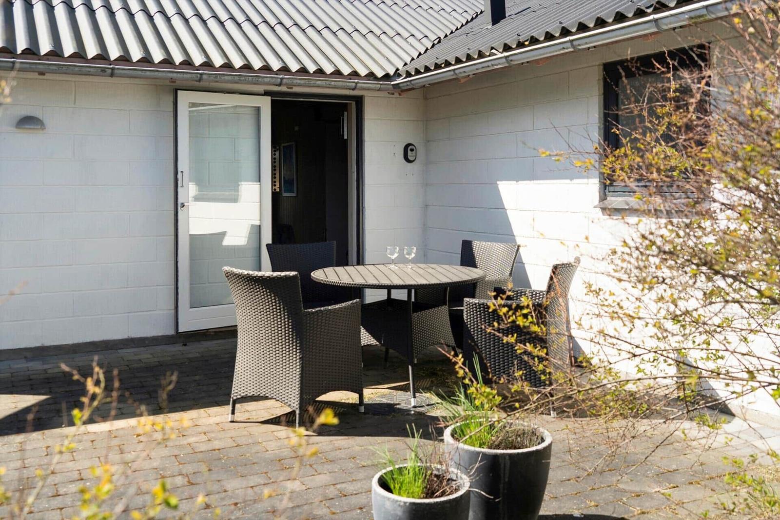 Terrasse mit Tisch und Stühlen vor einem weißen Haus mit Schiebetür.
