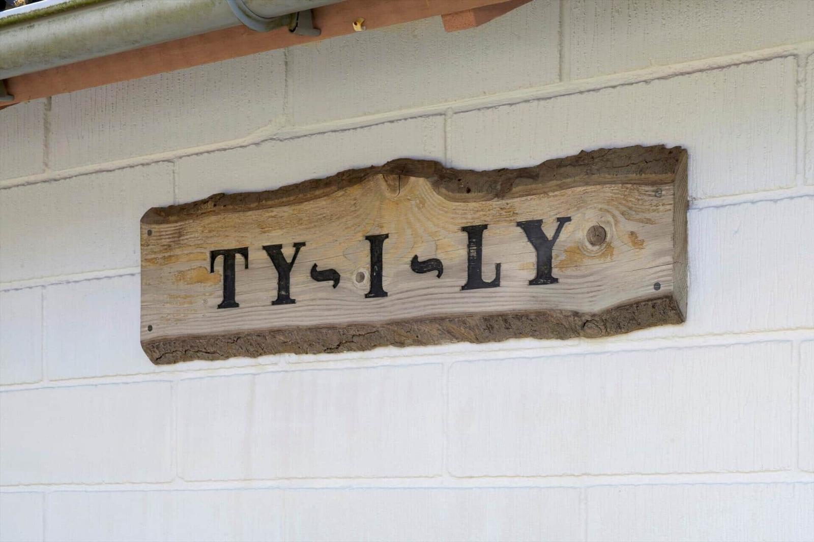 Holzschild mit der Aufschrift TY-I-LY an einer weißen Ziegelwand.
