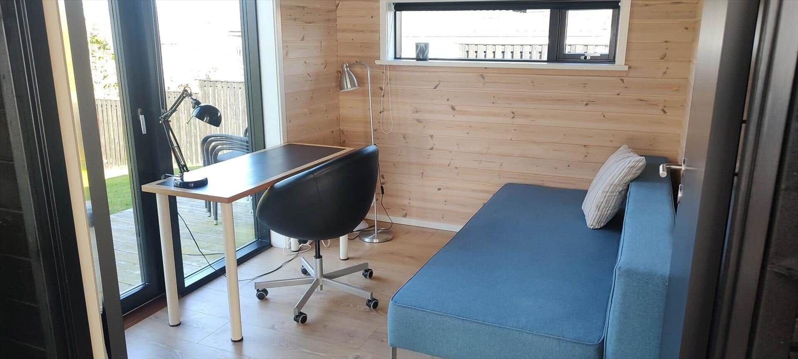 Ein Raum mit Schreibtisch, Stuhl und Sofa. Holzwand und Fenster.