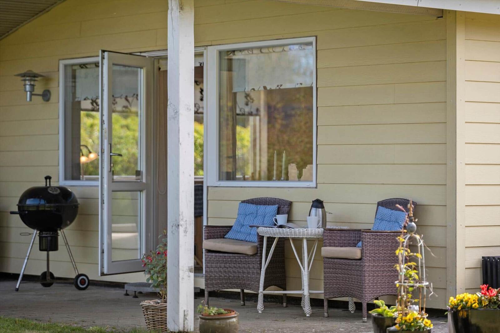 Patio with seating, grill, and flowers in front of yellow house.
