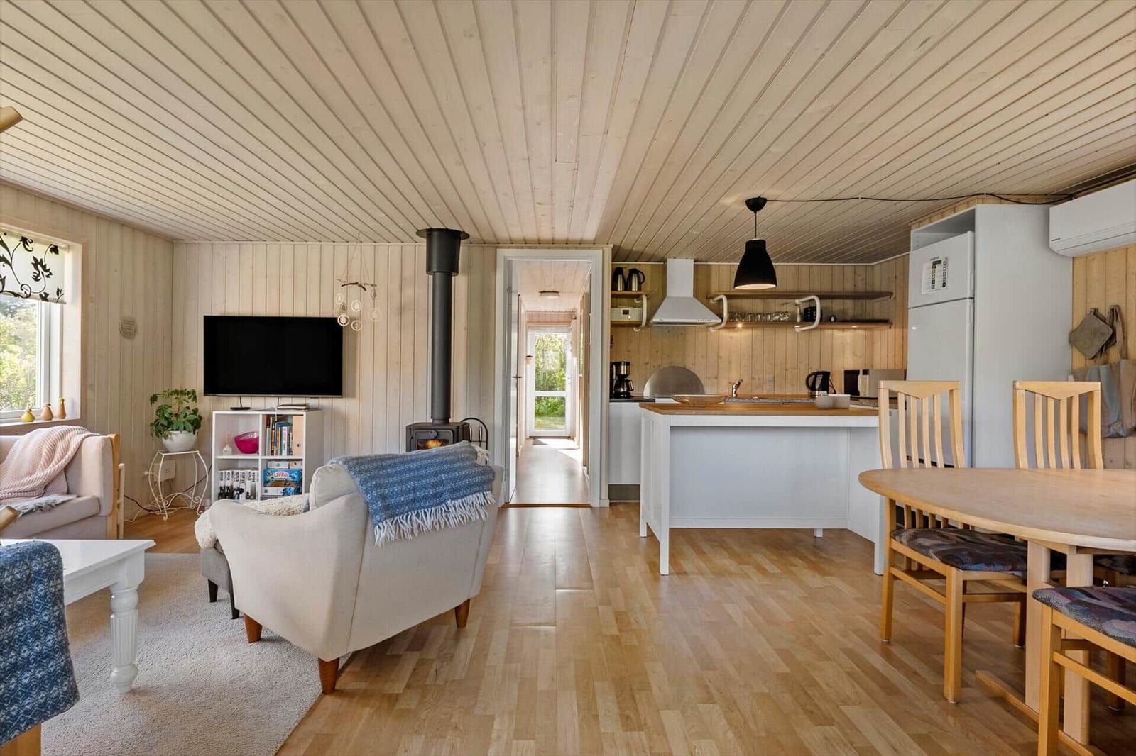 Living area with kitchen and dining table. Wooden ceiling, floor, and wood stove.