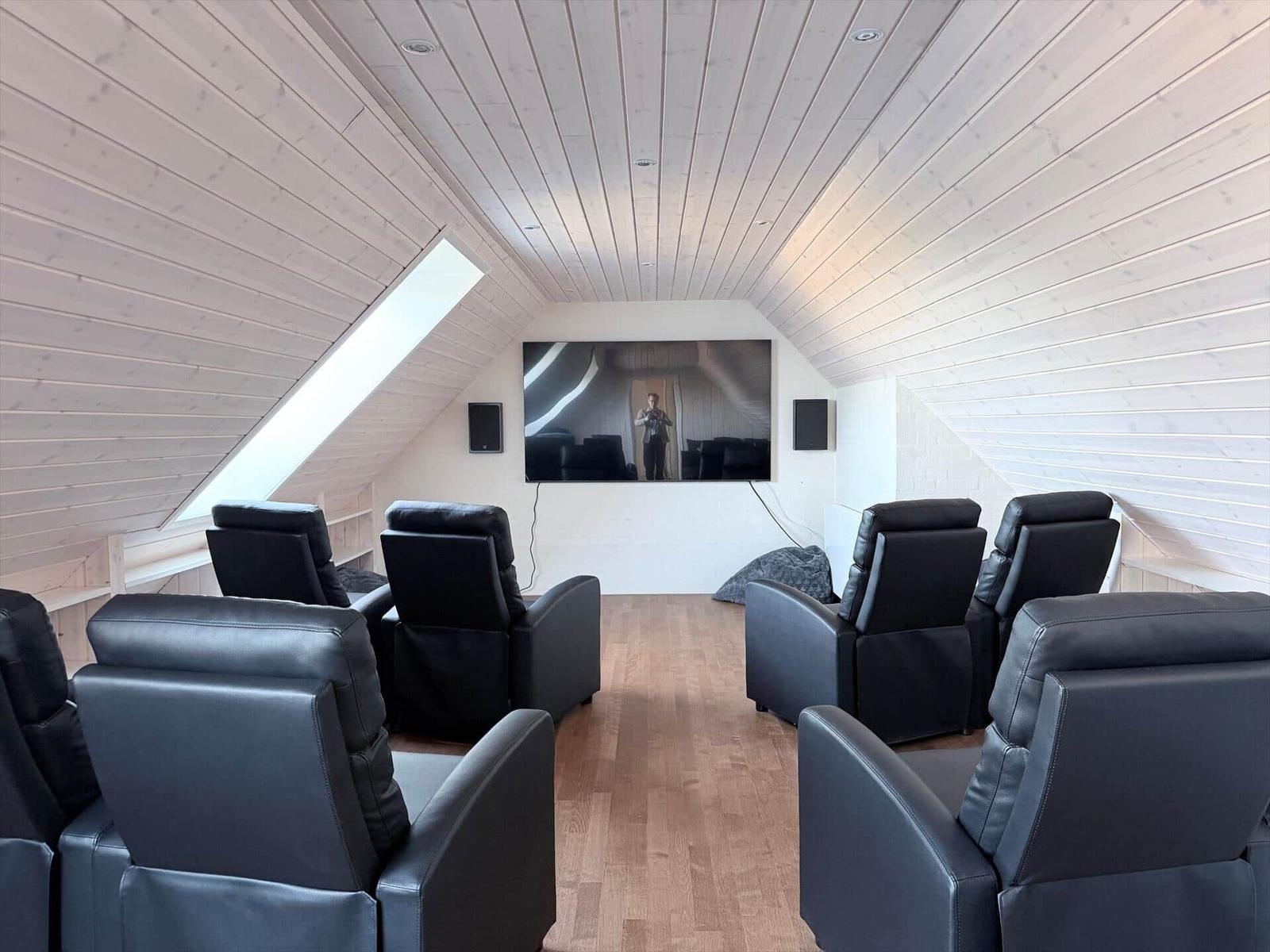 Dachgeschosszimmer mit schwarzen Sesseln, Holzboden und großem Bildschirm an der Wand.