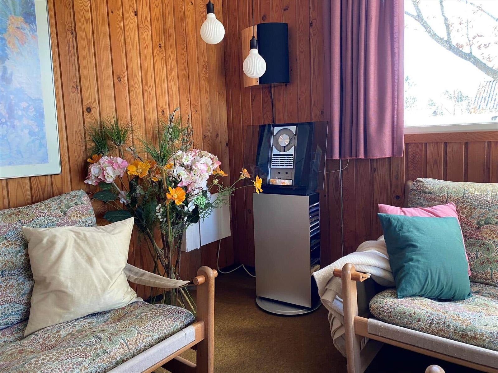 Zwei Sessel mit Kissen, Blumenstrauß, Wandlampe und Fenster mit Vorhang.