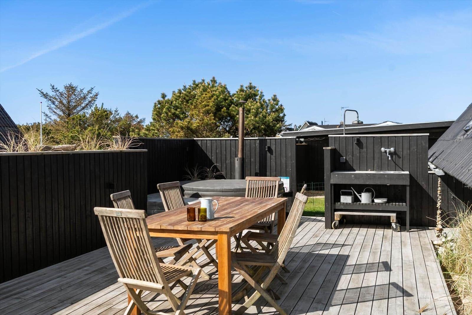 Holztisch mit Stühlen, Whirlpool und Grillbereich auf Holzterrasse.