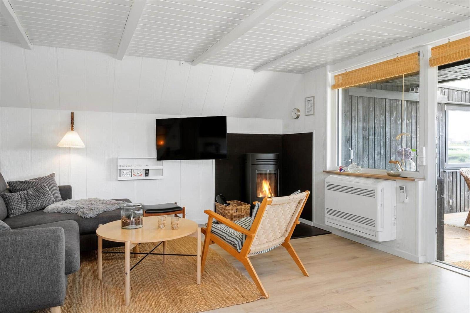 Wohnzimmer mit Sofa, Fernseher und Kamin. Holzfußboden und weiße Wände.
