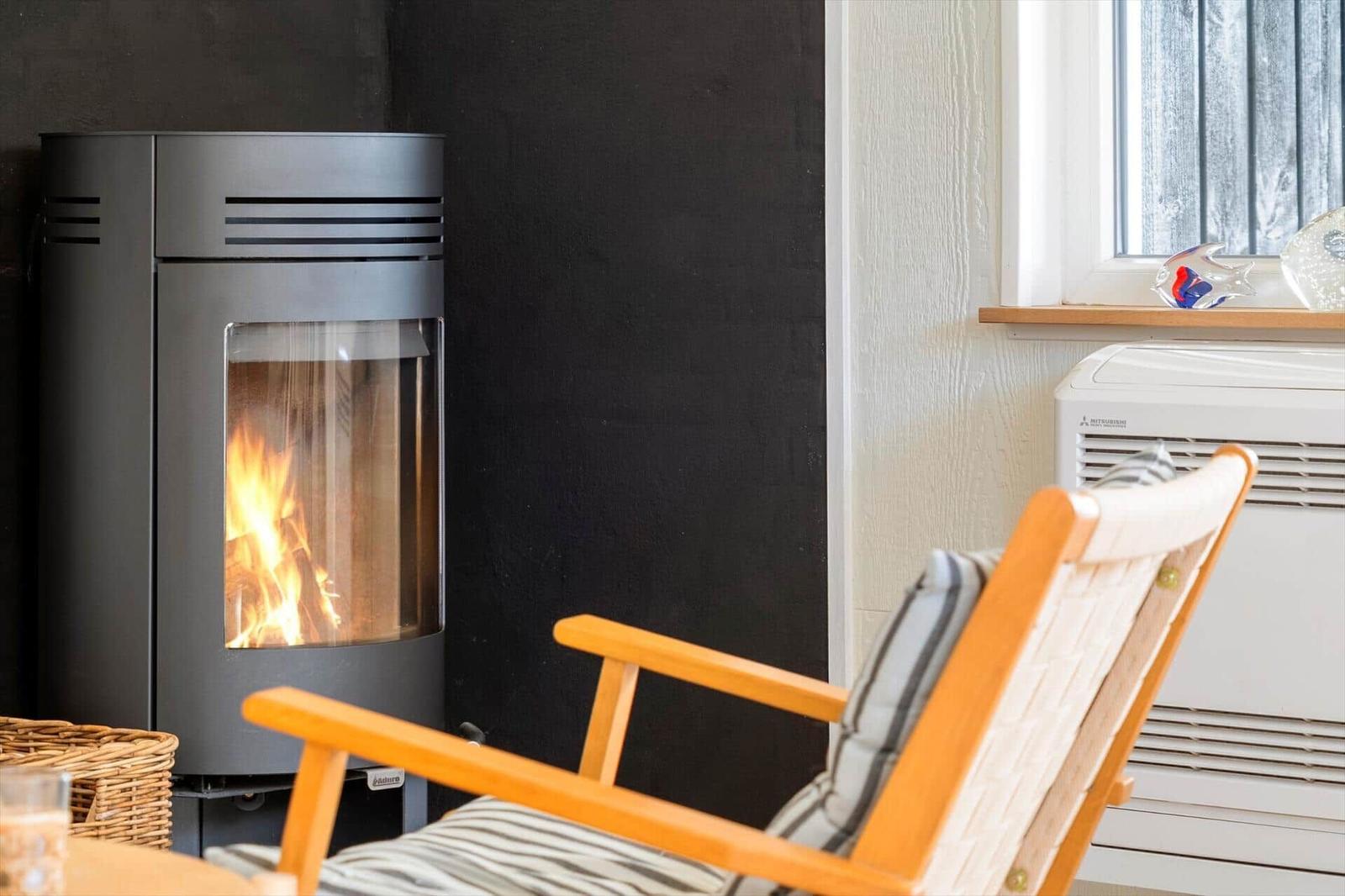 Ein Kaminofen mit brennendem Feuer neben einem Holzstuhl mit Kissen.