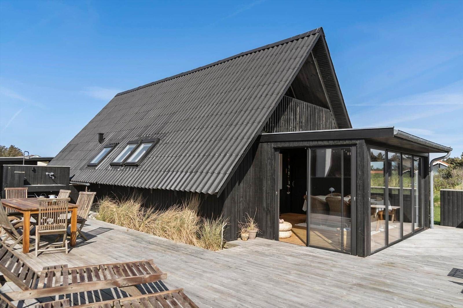 Moderne Holzhütte mit großem Holzterrasse und Glasveranda. Außentisch mit Stühlen.