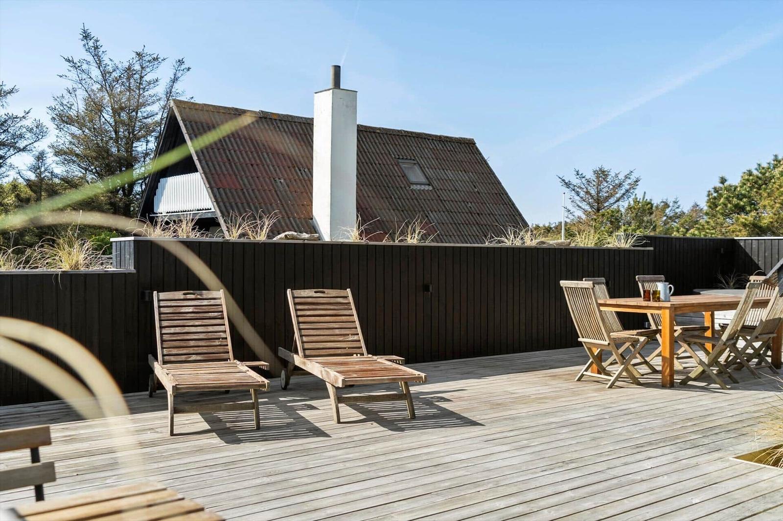 Terrasse mit Liegestühlen und Tisch. Hintergrund: Holzhaus mit Schornstein.