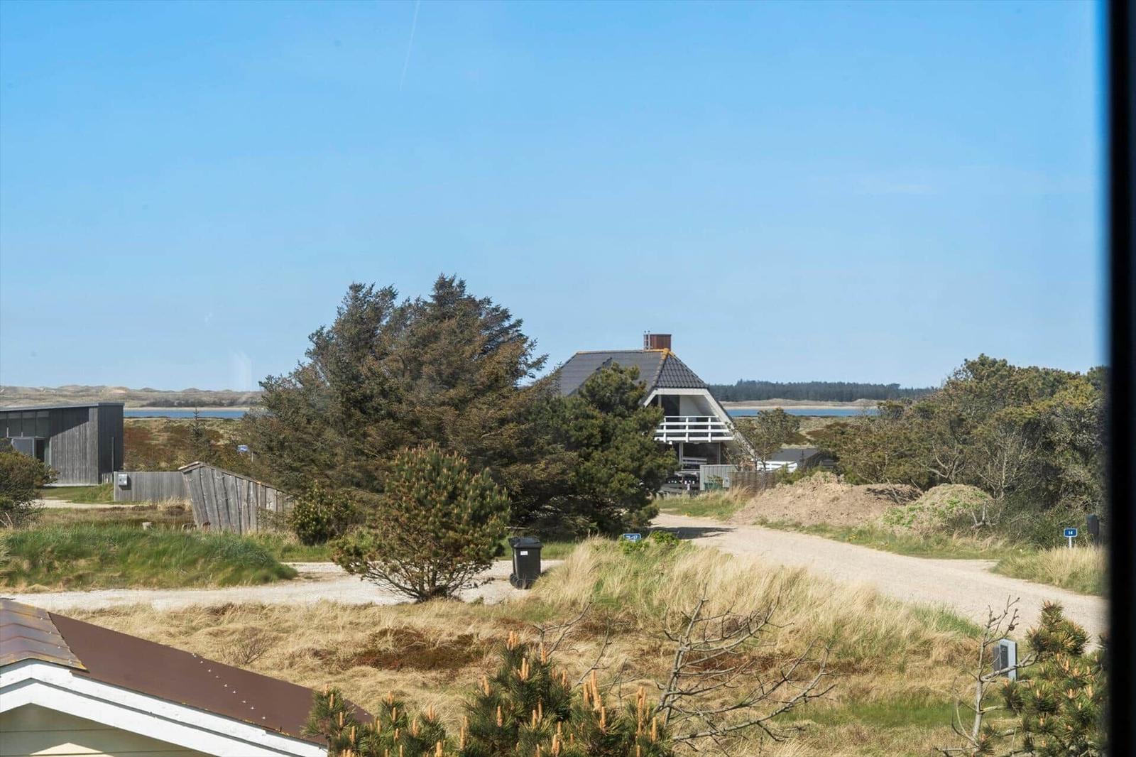 Haus mit Balkon, umgeben von Bäumen und Grasland unter blauem Himmel.