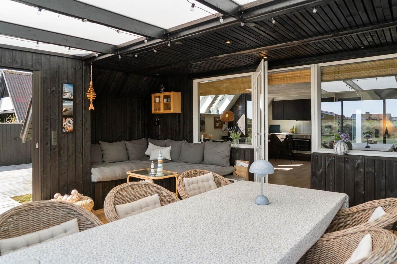 Terrasse mit Sitzgruppe, Esstisch und Blick ins Haus. Holzwände und offene Küche.