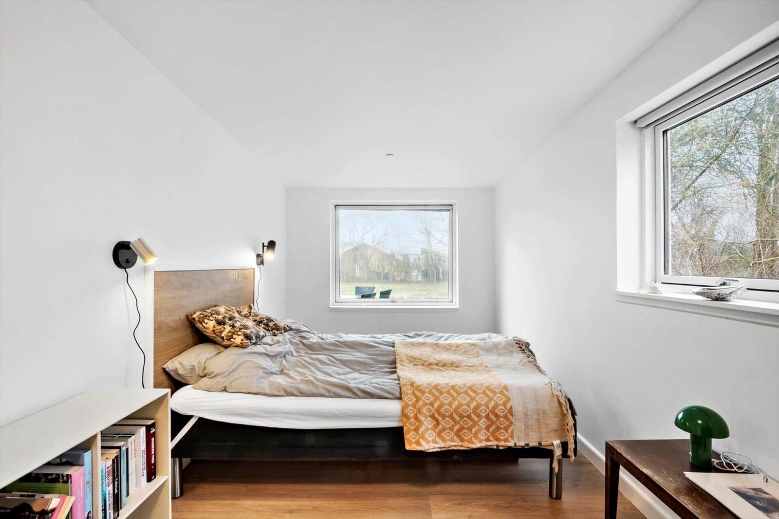 Schlafzimmer mit Bett, Fenstern und Holzboden.