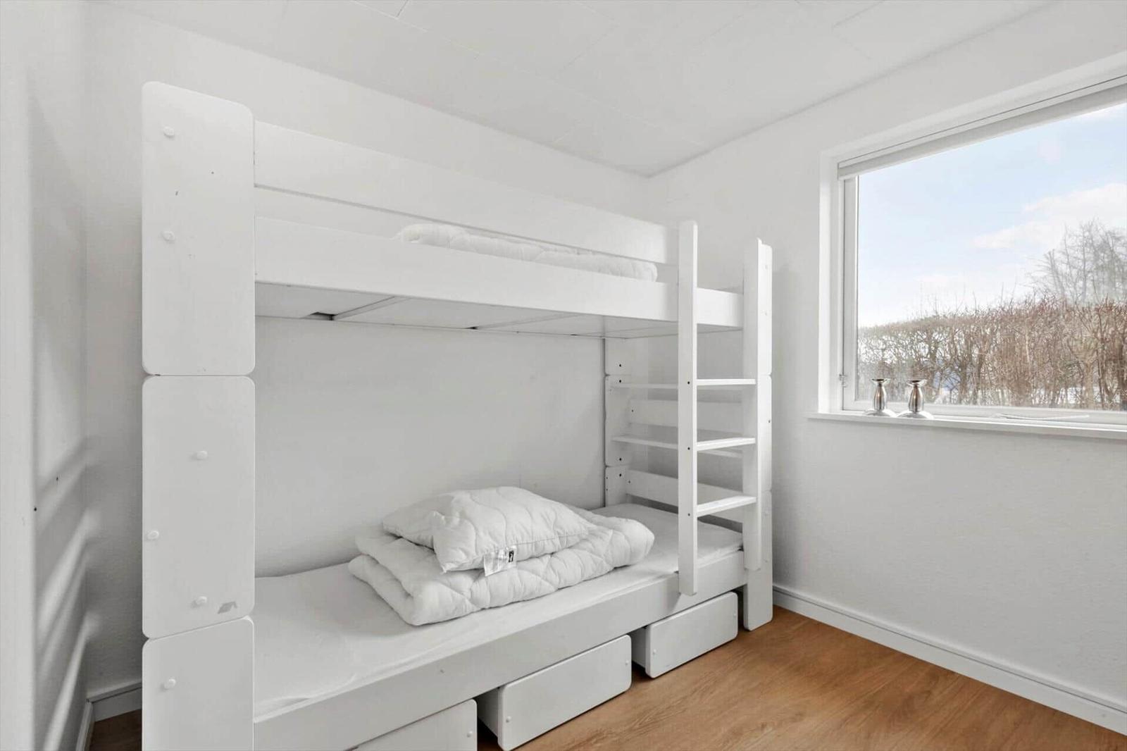 Ein Schlafzimmer mit weißen Doppelstockbetten und einem Fenster mit Blick auf Bäume.