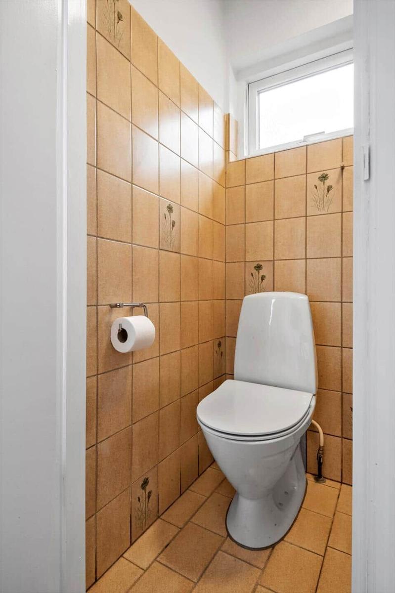 Toilette mit braunen Fliesen und Toilettenpapierhalter