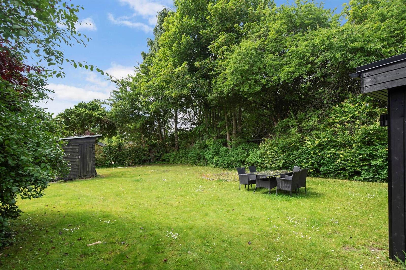 Garten mit Rasenfläche, Sitzgruppe und Holzschuppen. Umgeben von Bäumen und Sträuchern.