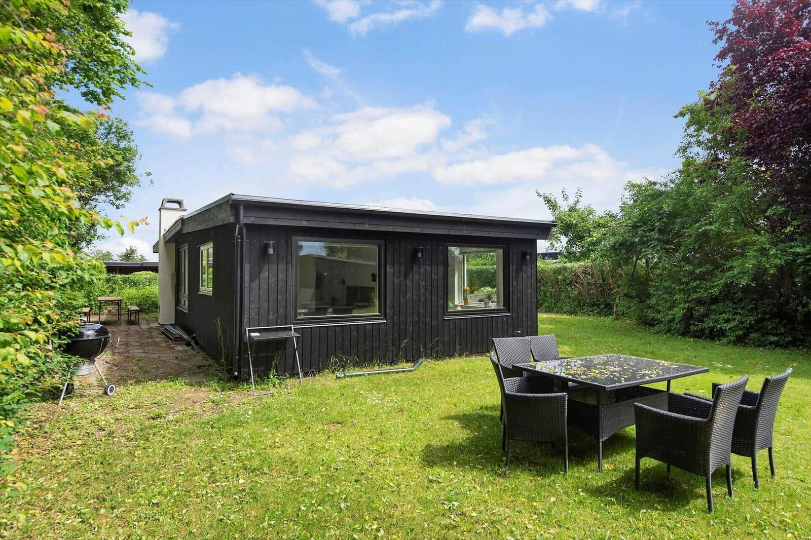 Schwarzes Holzhaus mit Garten, Sitzgruppe und Grill. Hinterhof mit Bäumen.