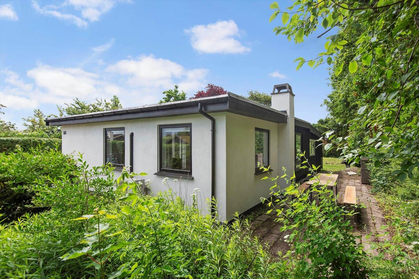 Ein weißes Haus mit dunklen Fensterrahmen und einem Gartenweg mit Holztisch.