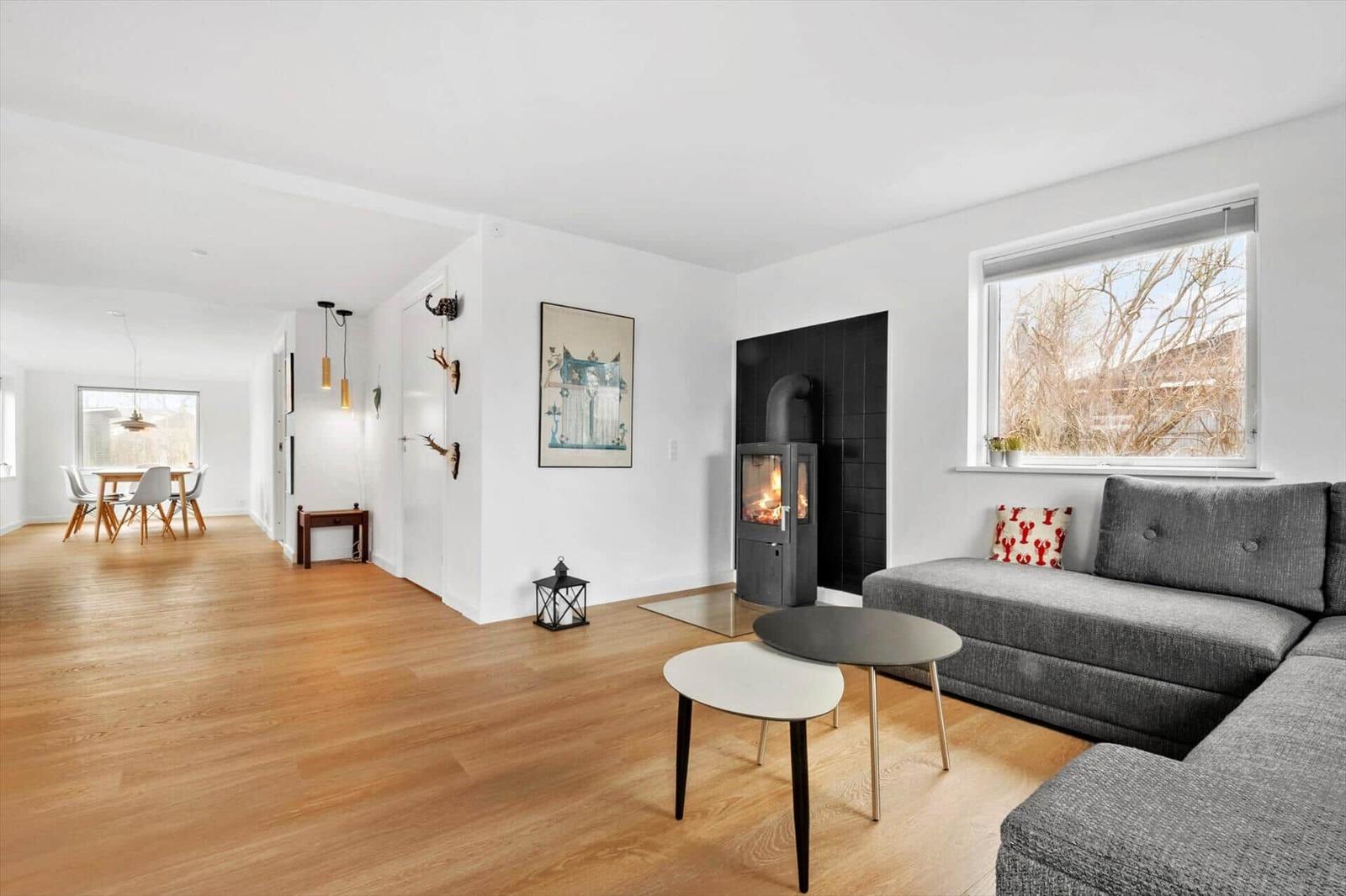 Wohnbereich mit grauem Sofa, Kamin und Holzboden. Durchgang zur Essnische mit Tisch und Stühlen.