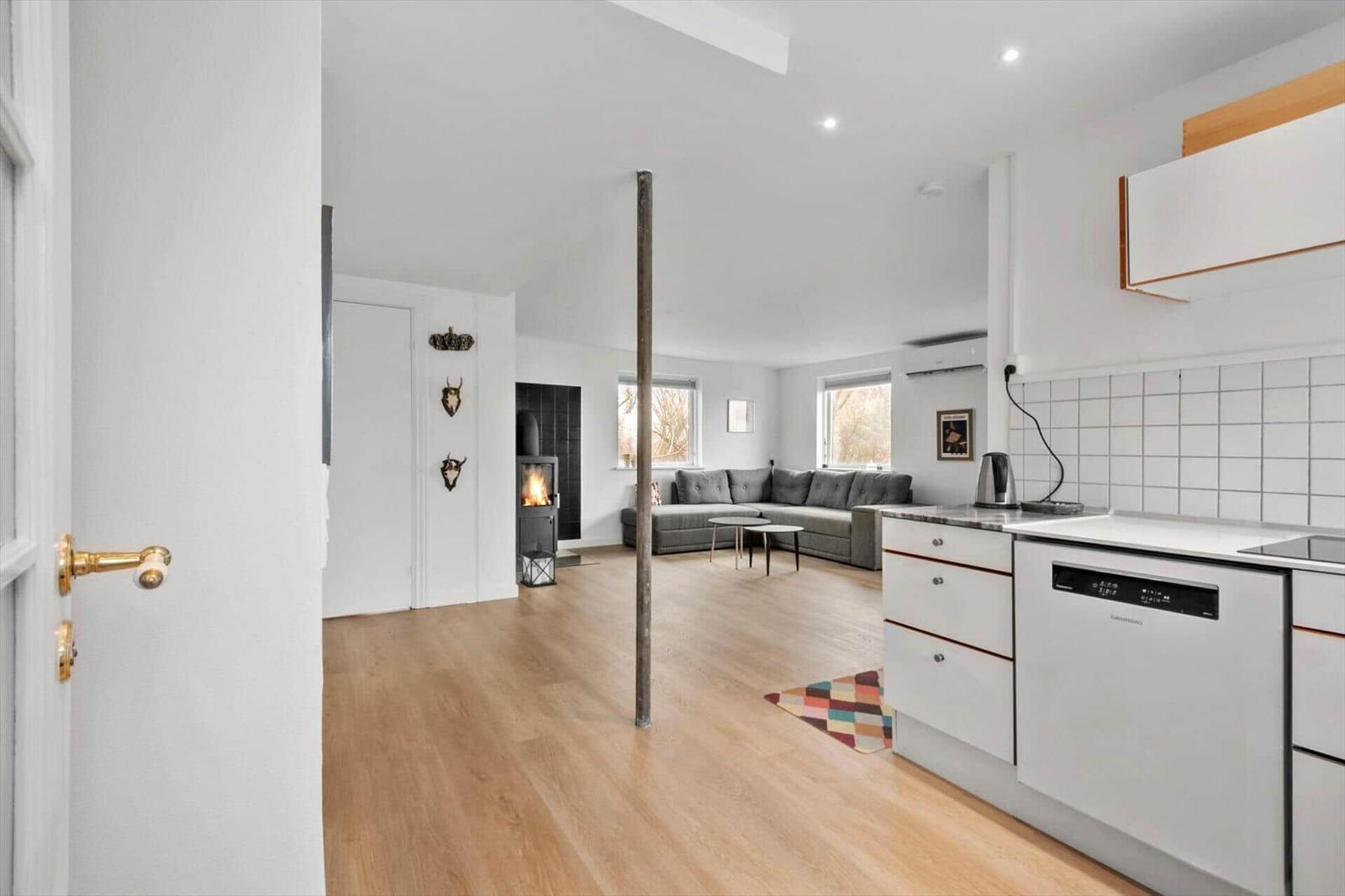 Küche mit weißen Schränken und Wohnbereich mit grauem Sofa und Kamin.