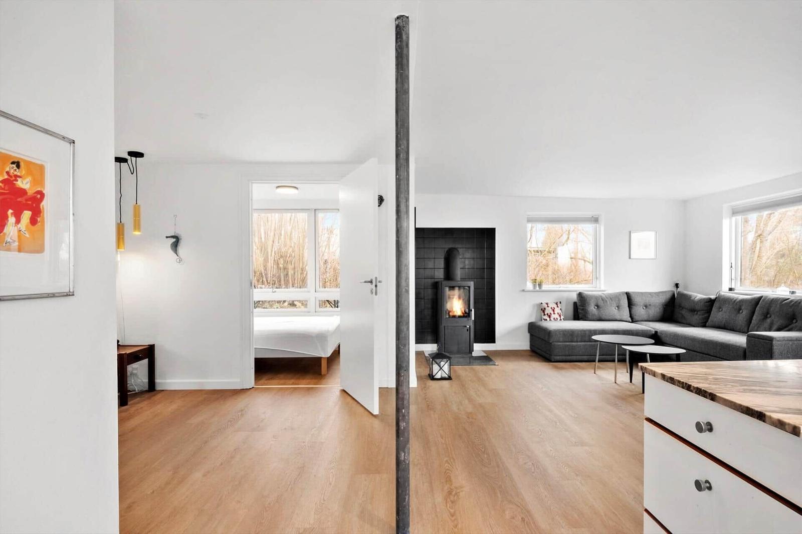 Wohnbereich mit Kamin und grauem Sofa. Durchgang zur Schlafzimmer mit Bett.