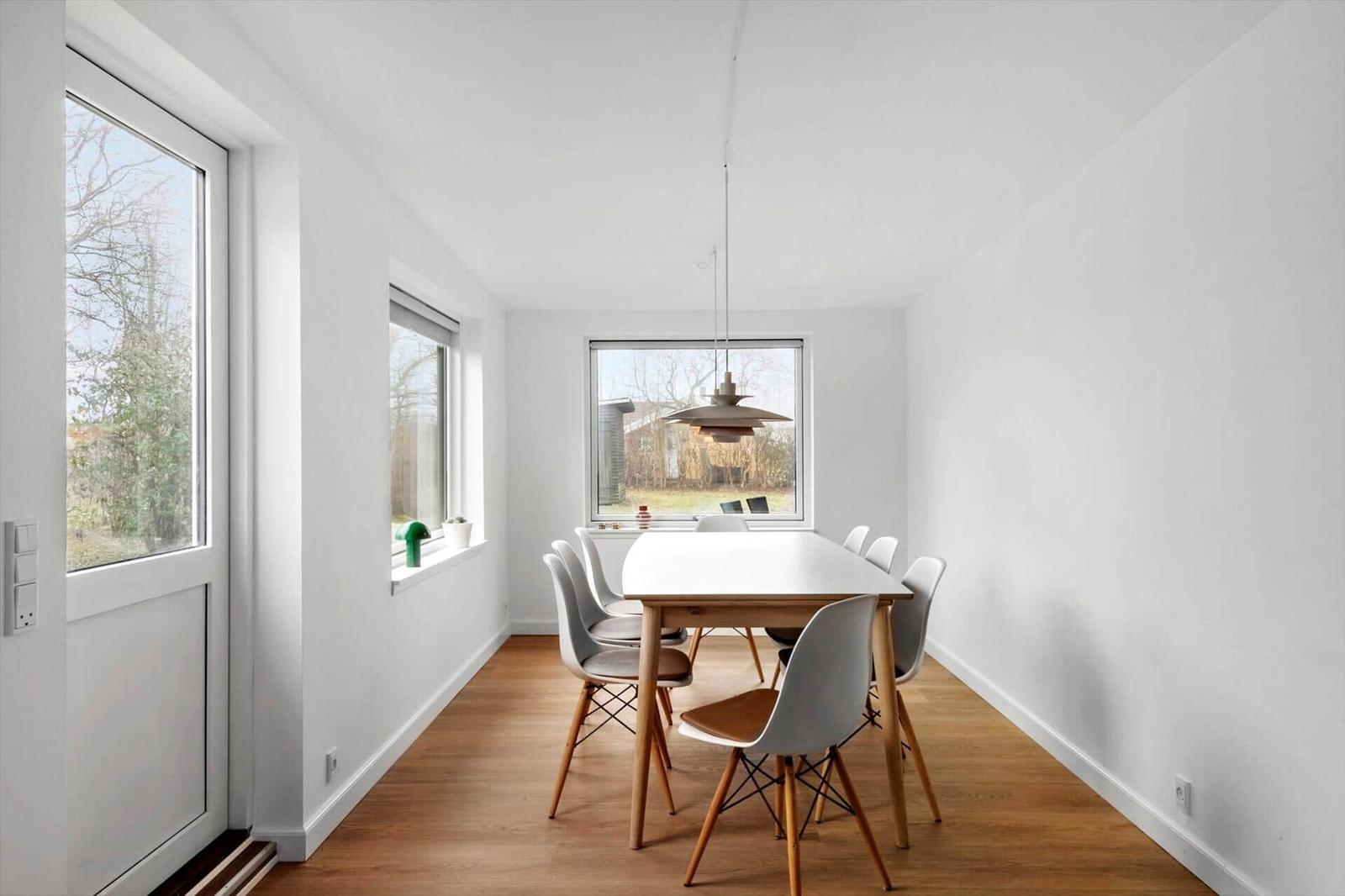 Esszimmer mit Holztisch, sechs Stühlen und großen Fenstern.