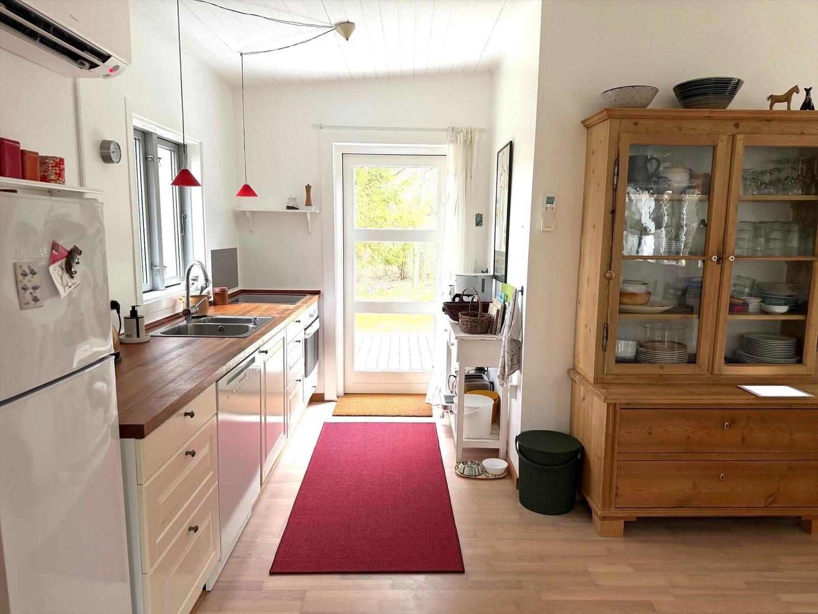 Küche mit Holzoberfläche, Kühlschrank und Glasvitrine. Tür führt nach draußen.