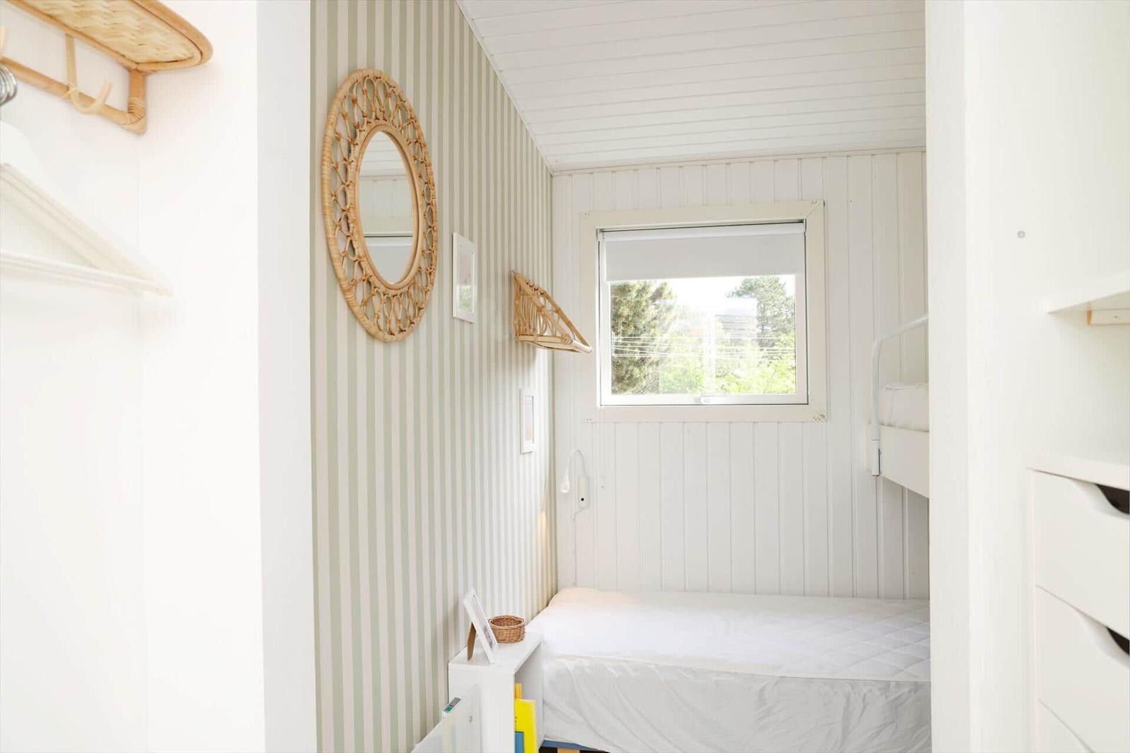 Schlafzimmer mit Bett, Fenster und Streifenwand. Wandspiegel und Regal sichtbar.