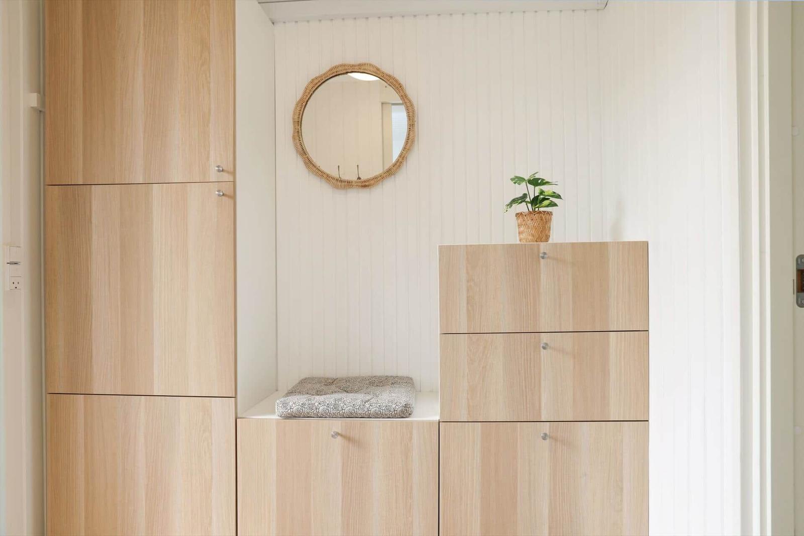 Hölzerner Schrank mit Sitzfläche, runder Spiegel und Pflanze auf Kommode