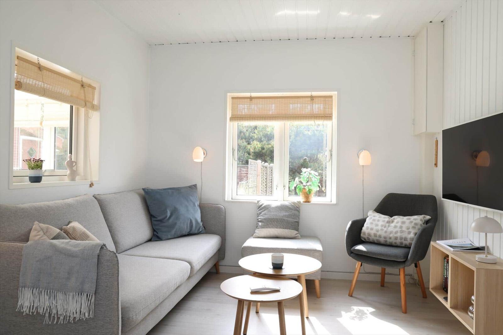 Wohnzimmer mit Sofa, Sessel, zwei Tischen und Fenstern mit Jalousien.