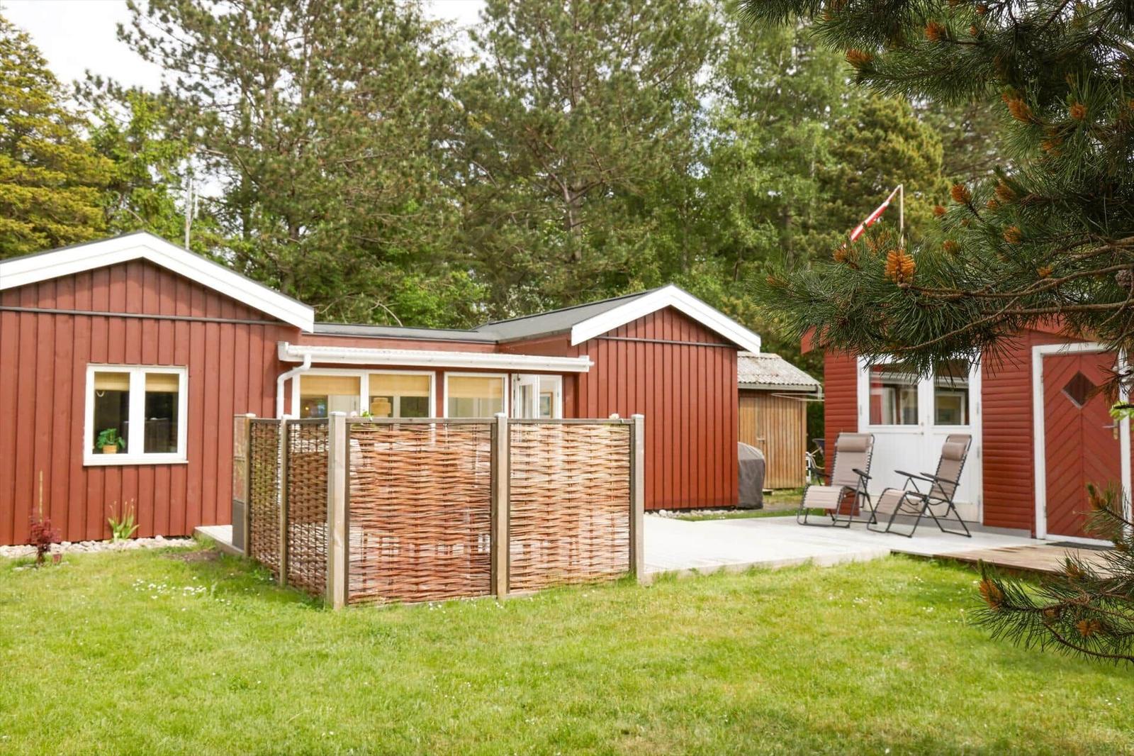 Roter Holzhaus mit Terrasse und Sitzgelegenheiten im Grünen.