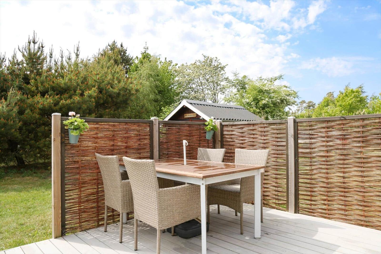 Terrasse mit Tisch und Stühlen, umgeben von einem Hainbuchenzaun und Grünflächen.