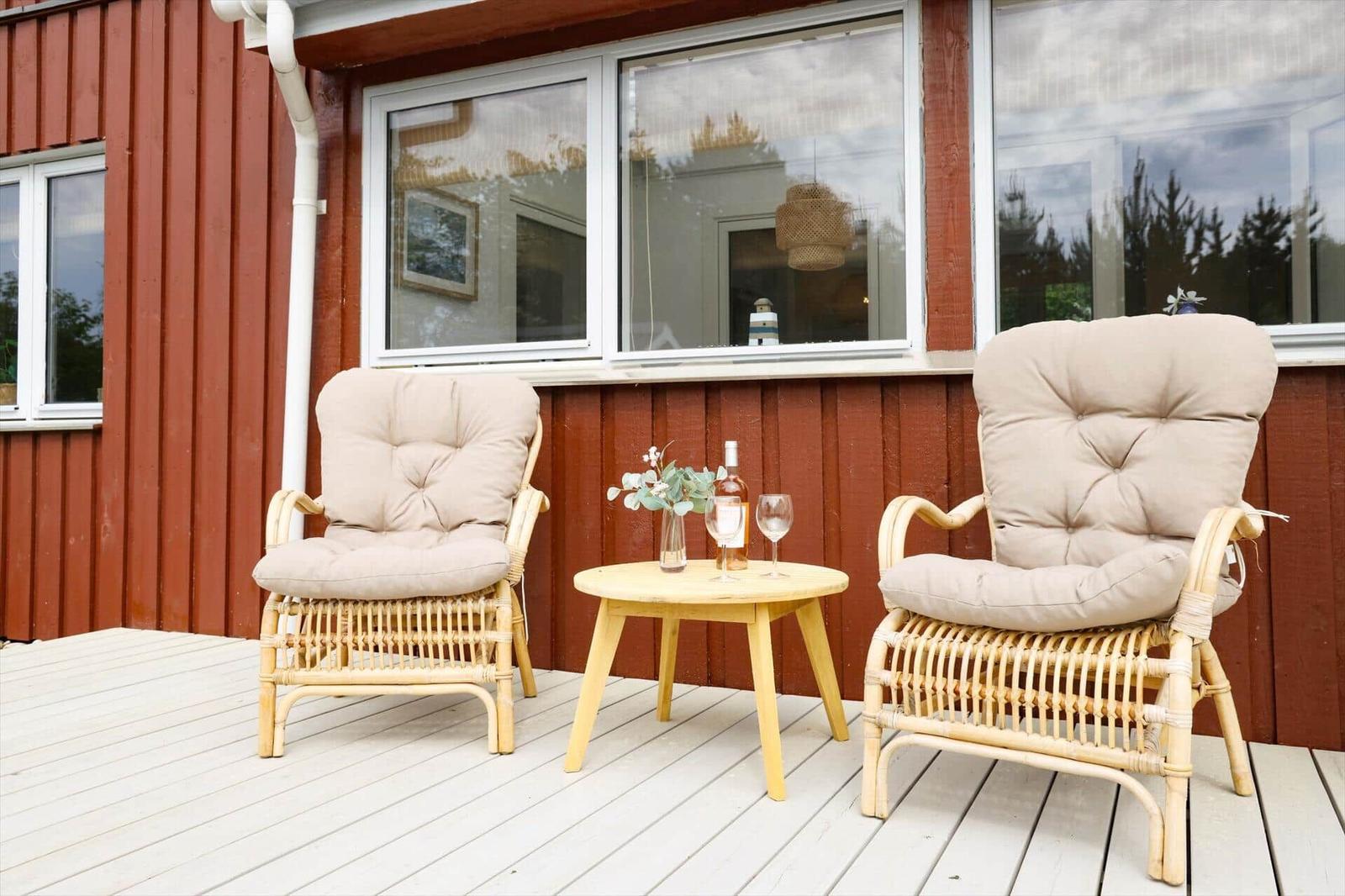 Zwei Rattan-Stühle mit Kissen und kleiner Tisch auf Terrasse vor rotem Haus.