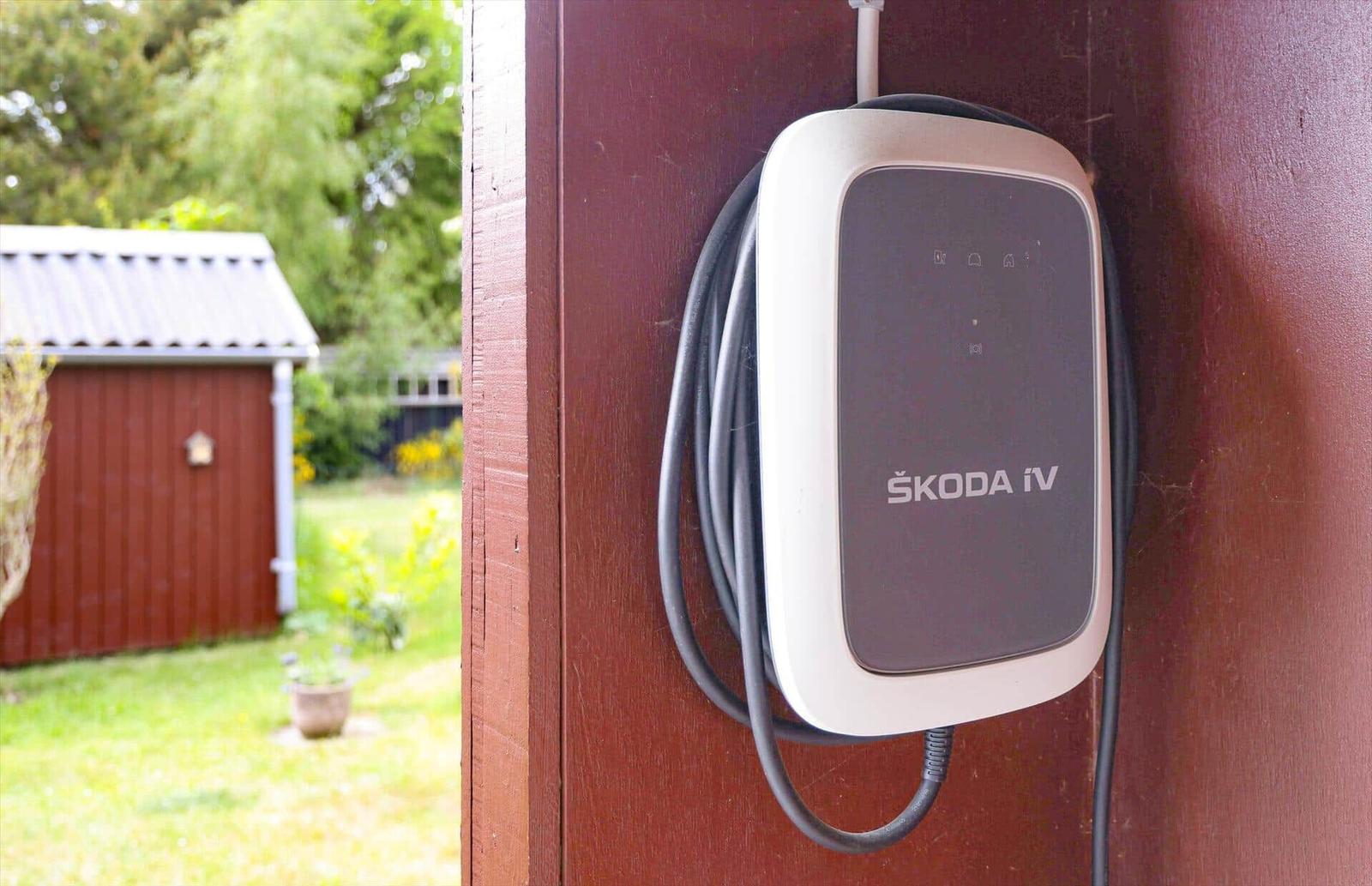 Ladestation an Wand montiert, im Hintergrund Garten und Schuppen.
