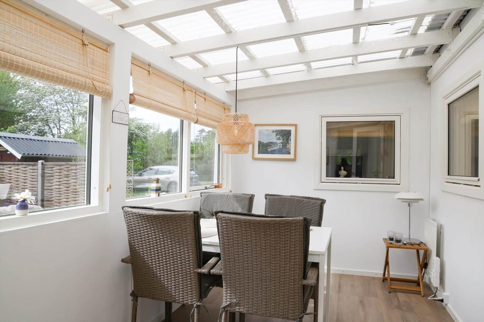 Essbereich mit Tisch, Stühlen und Glasdach. Fenster mit Jalousien und Wandbild.