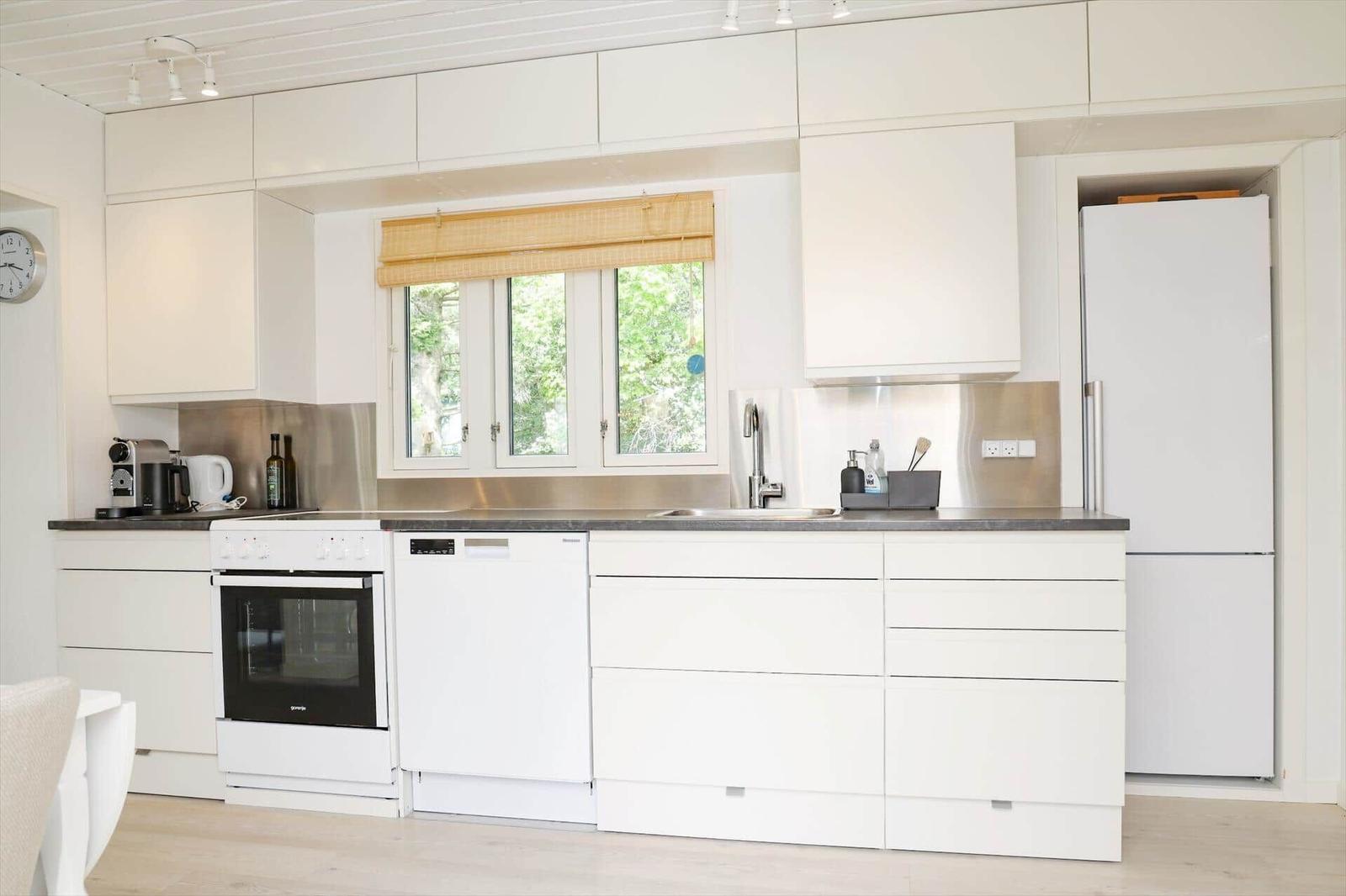 Küche mit weißen Schränken, Edelstahlarbeitsplatte und Fenster mit Jalousie.