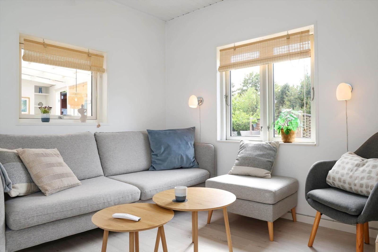 Wohnzimmer mit grauem Sofa, zwei Tischen und Fenstern mit Jalousien.