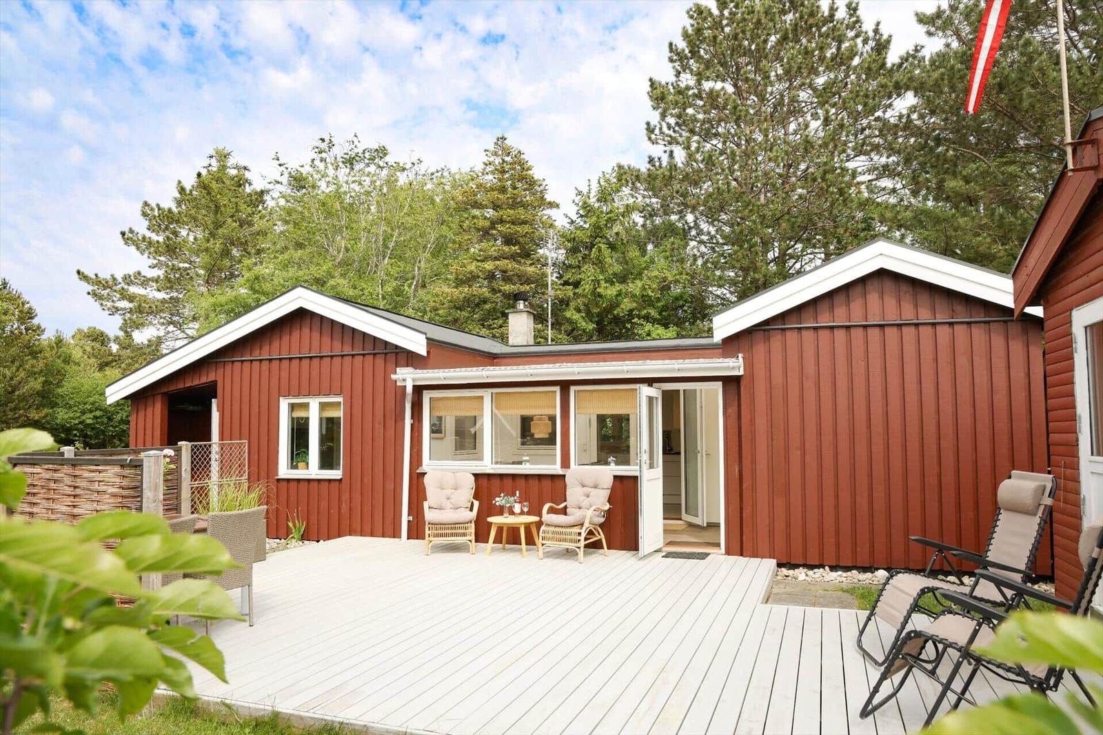 Rotes Holzhaus mit Terrasse und Sitzgelegenheiten im Grünen.