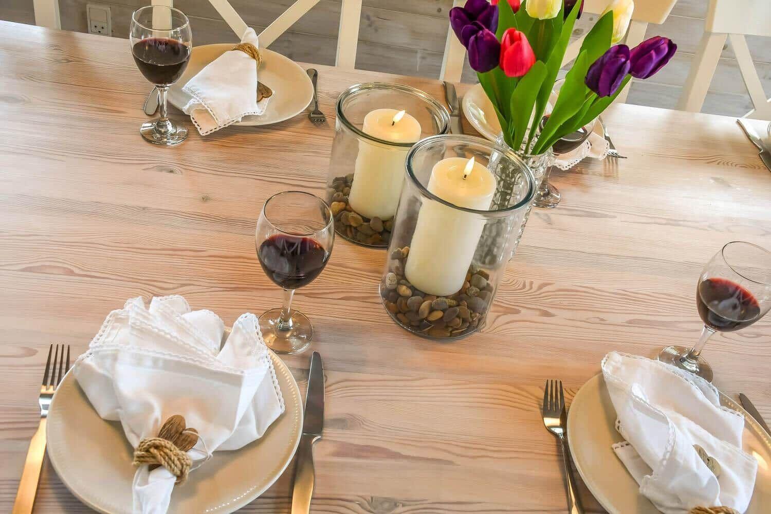 Holztisch mit gedeckten Plätzen, Kerzen und Tulpenblumen.
