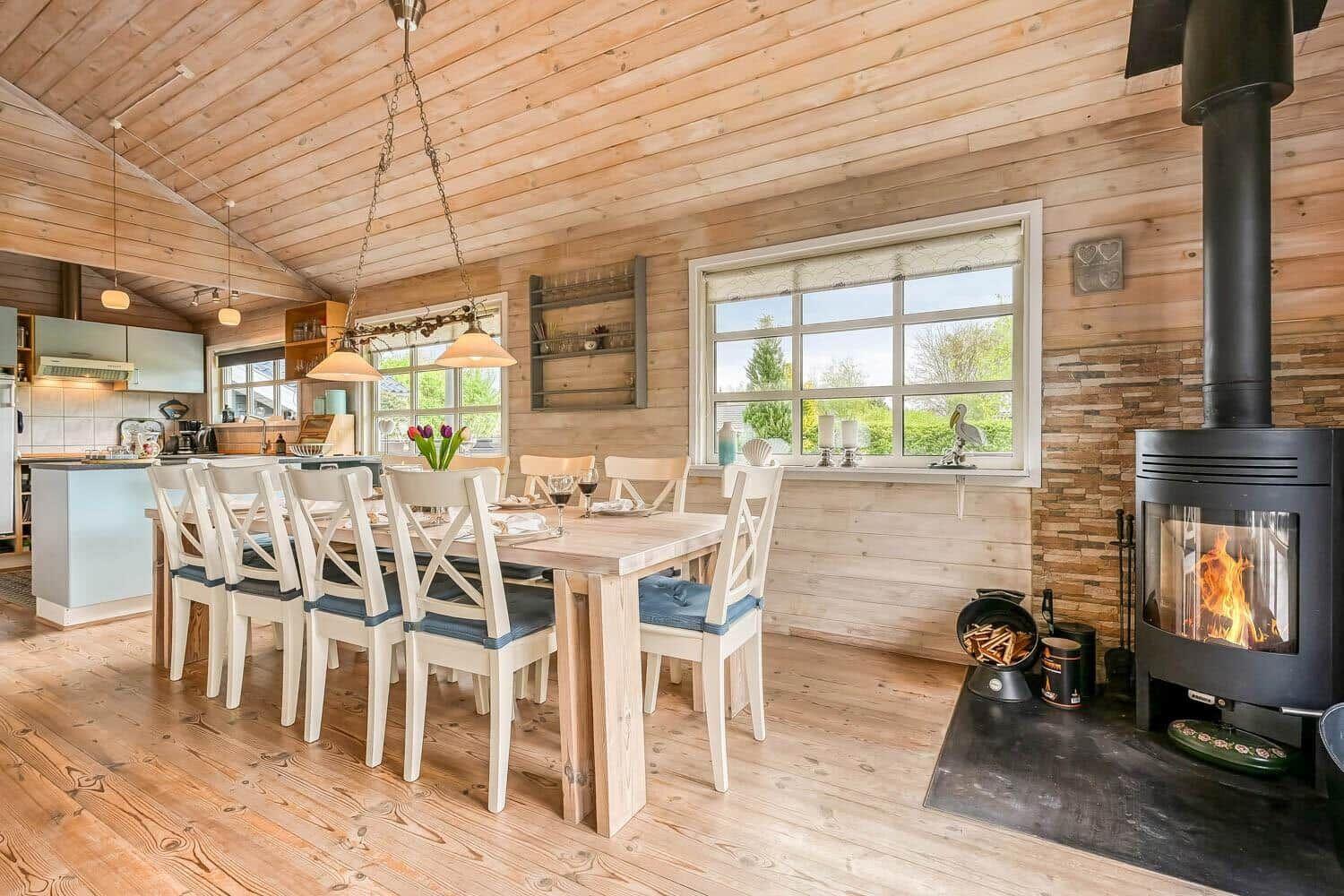 Holzgetäfelte Küche mit Esstisch, Kamin und Fensterblick auf Grün.