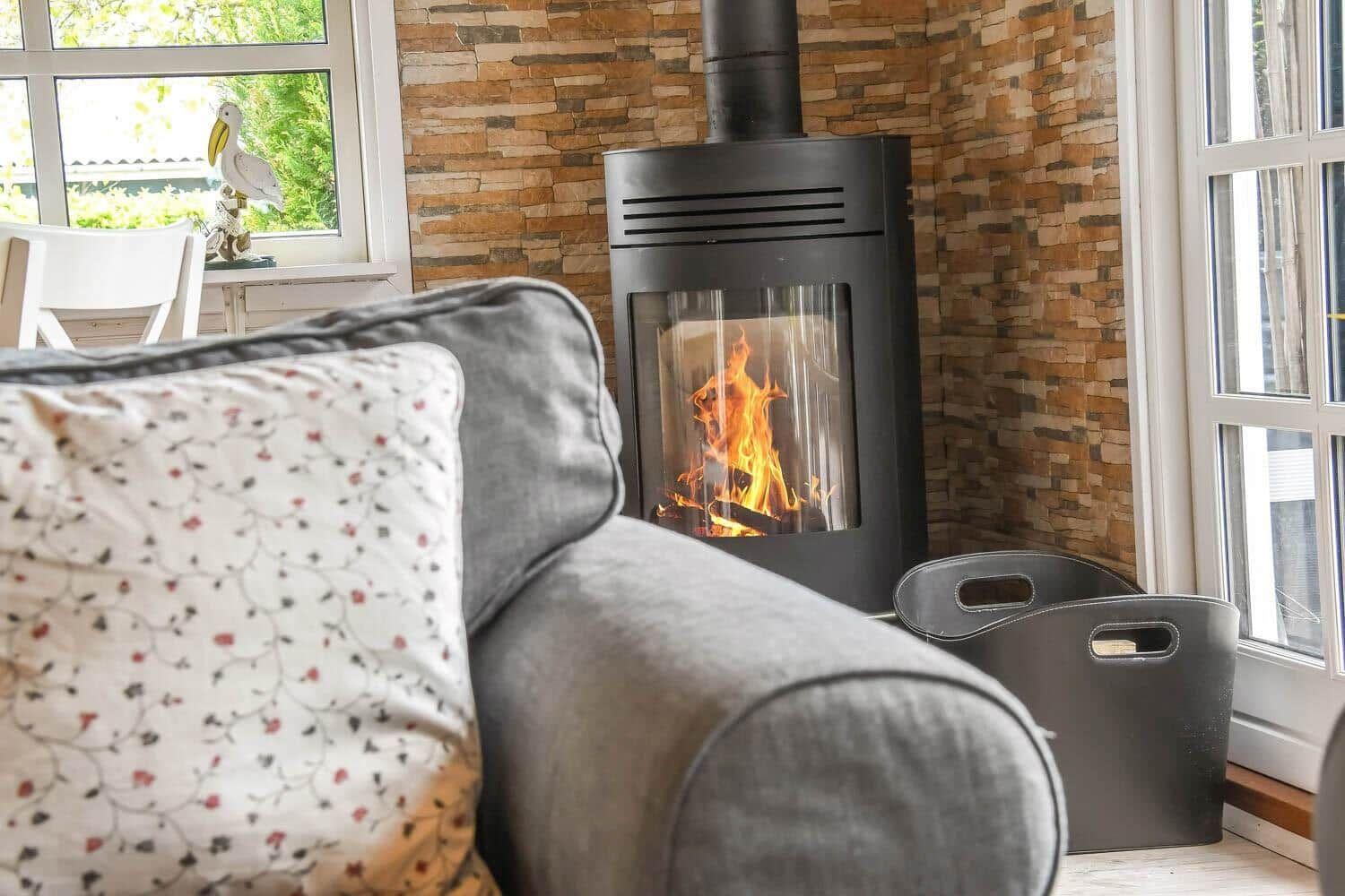 Ein grauer Sessel mit Kissen vor einem brennenden Kamin und Steinwand.