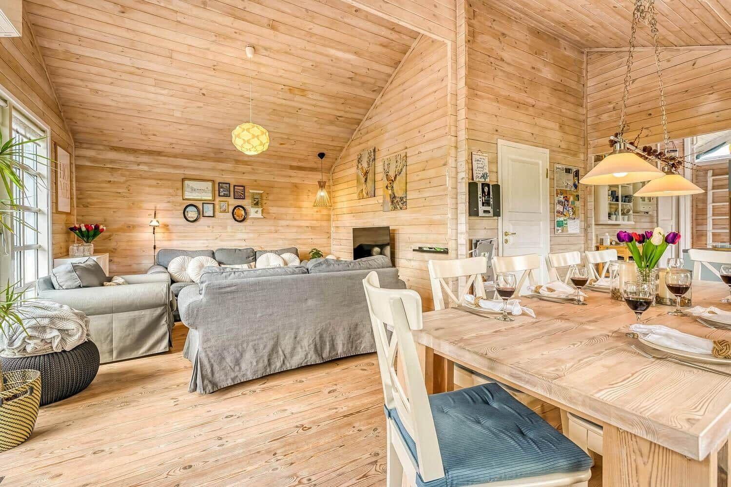 Wohn- und Essbereich mit Holzwand und -boden, Sofa, Esstisch und Lampen.