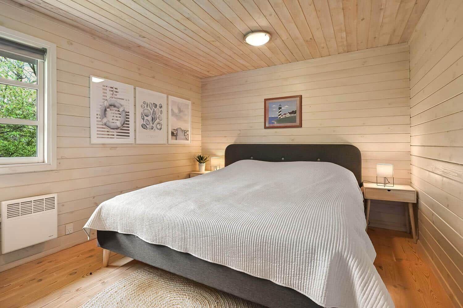 Schlafzimmer mit Bett, Nachttischen und Wandbildern. Holzwände und Boden.