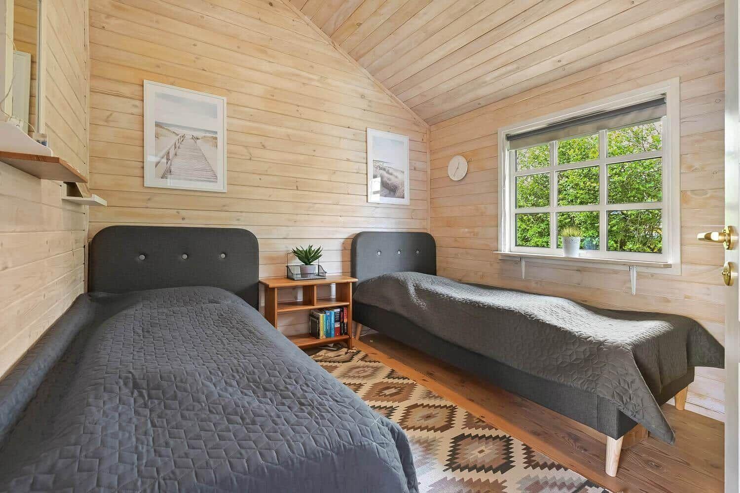 Zwei Einzelbetten in einem Holzhauszimmer mit Fenster und Wandbildern.