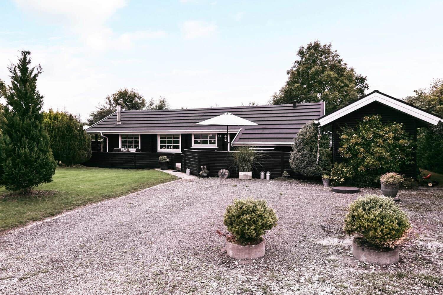 Schwarzes Haus mit Terrasse, Garten und Sonnenschirm. Grasfläche und Pflanzen.