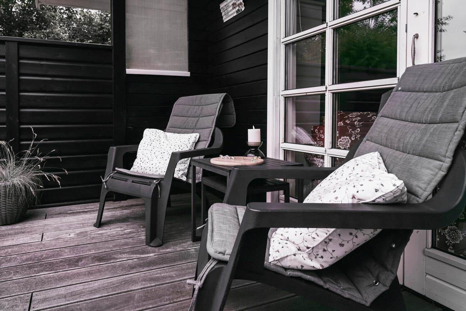 Terrasse mit zwei Sesseln, Tisch und Pflanze vor schwarzem Holzhaus.