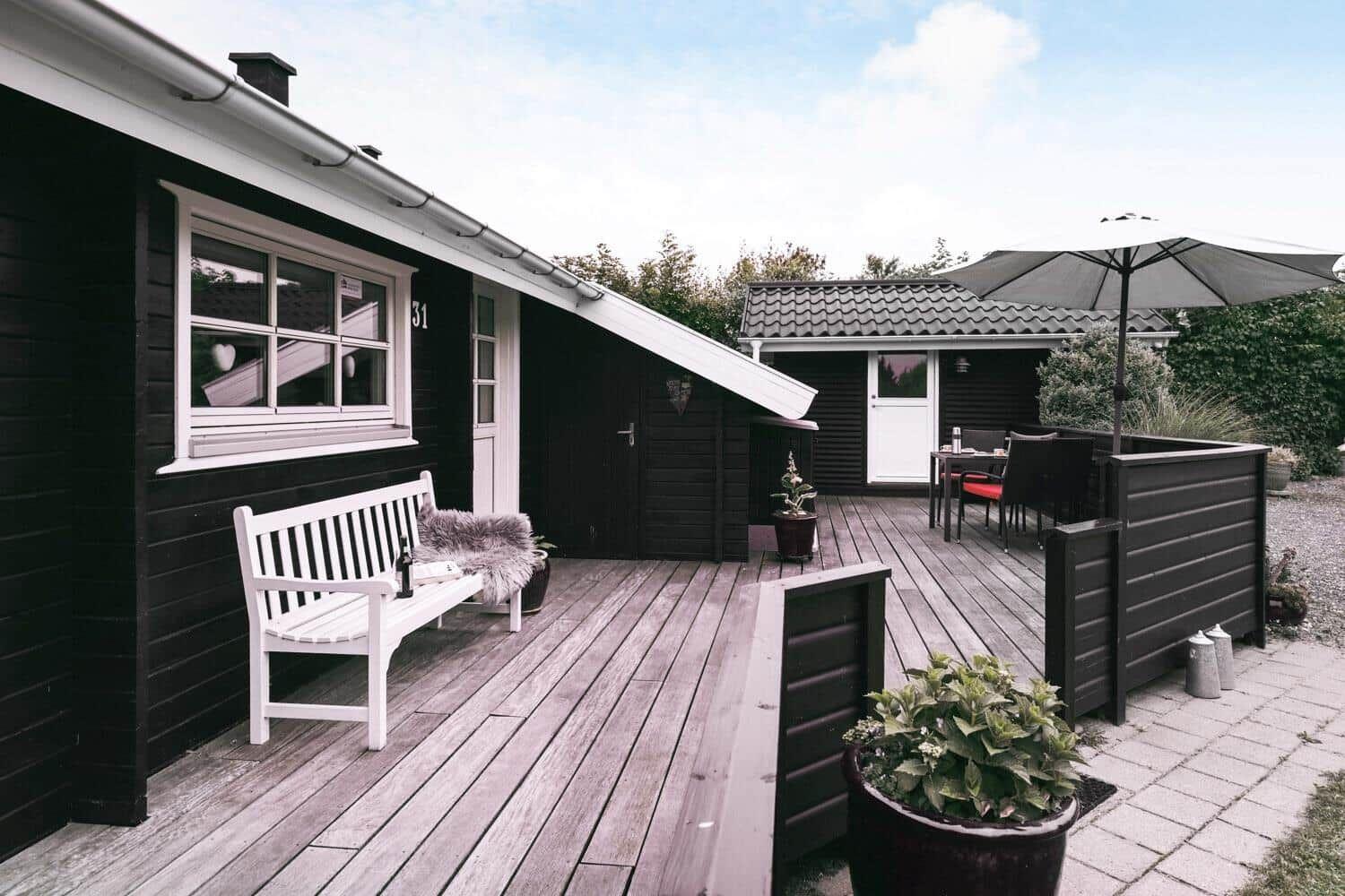 Terrasse mit weißem Bistroset und Sonnenschutz. Holzterrasse und Pflanzen sind sichtbar.