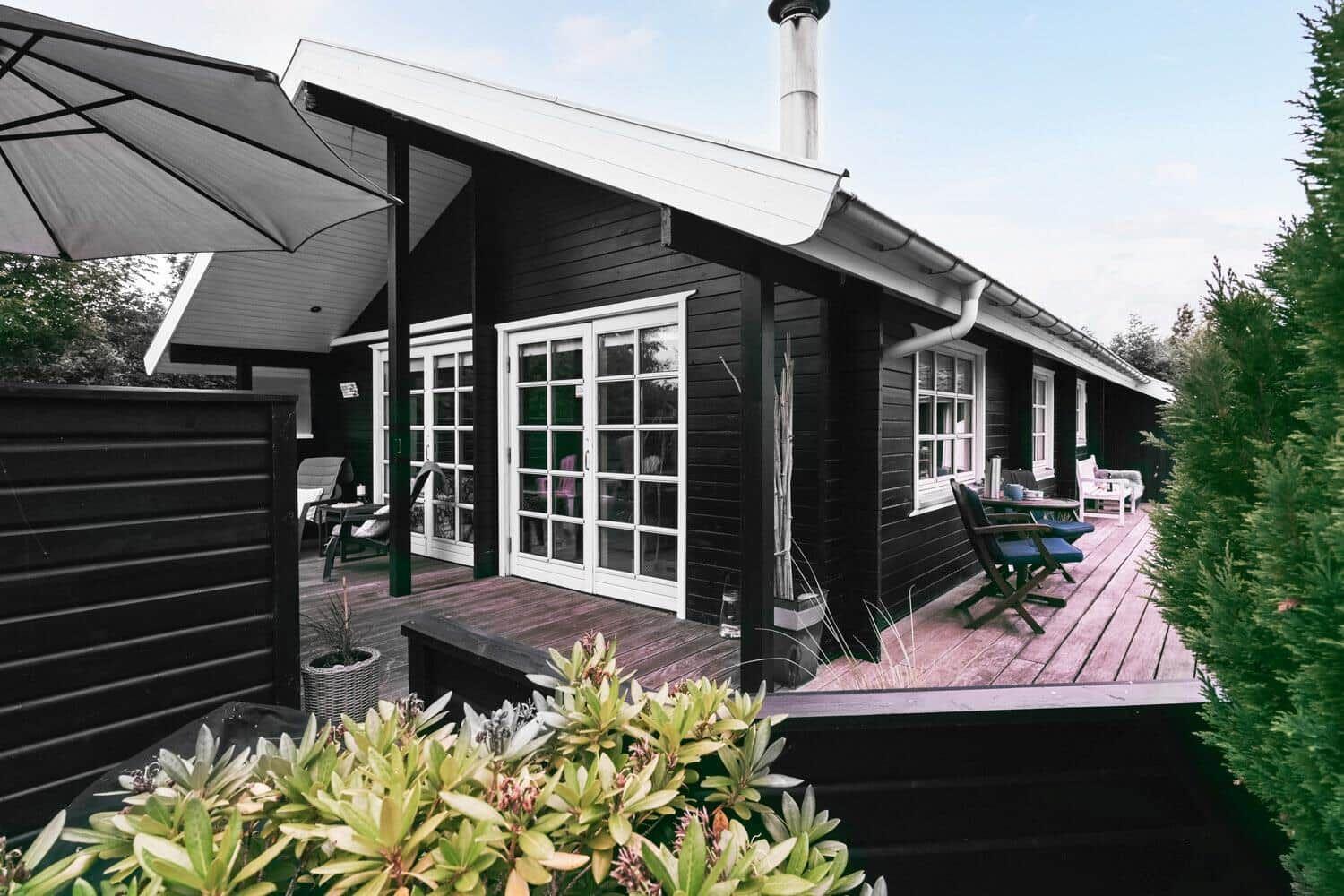 Schwarzes Holzhaus mit Terrasse, Gartenmöbeln und Sonnenschutz.
